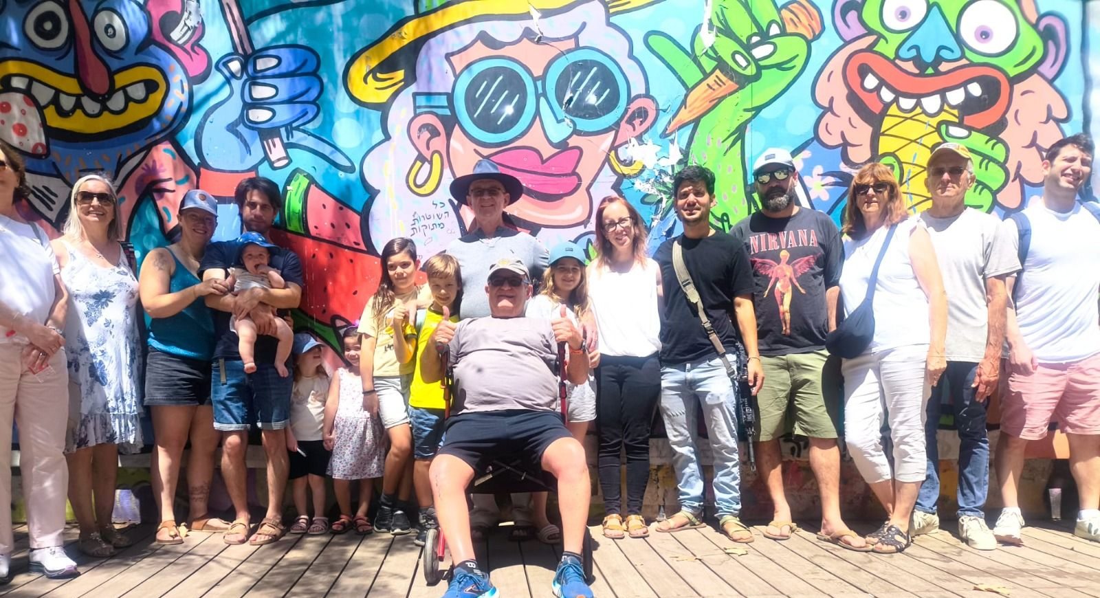 קבוצת משפחות עם ילדים מצטלמת מול ציור קיר ענק וצבעוני
