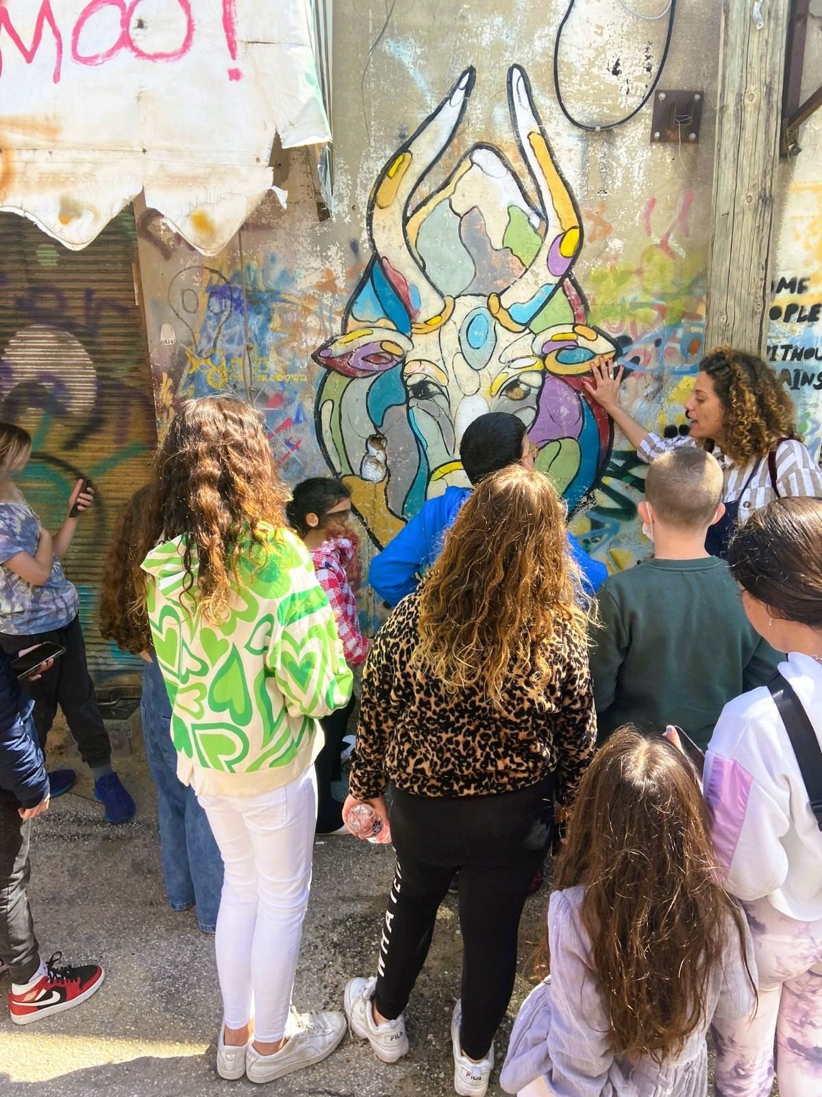קבוצת ילדים מקשיבה להסבר מול ציור של שור צבעוני על קיר